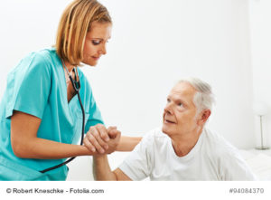 Frau im Pflegeheim hilft einem Senioren beim Aufstehen